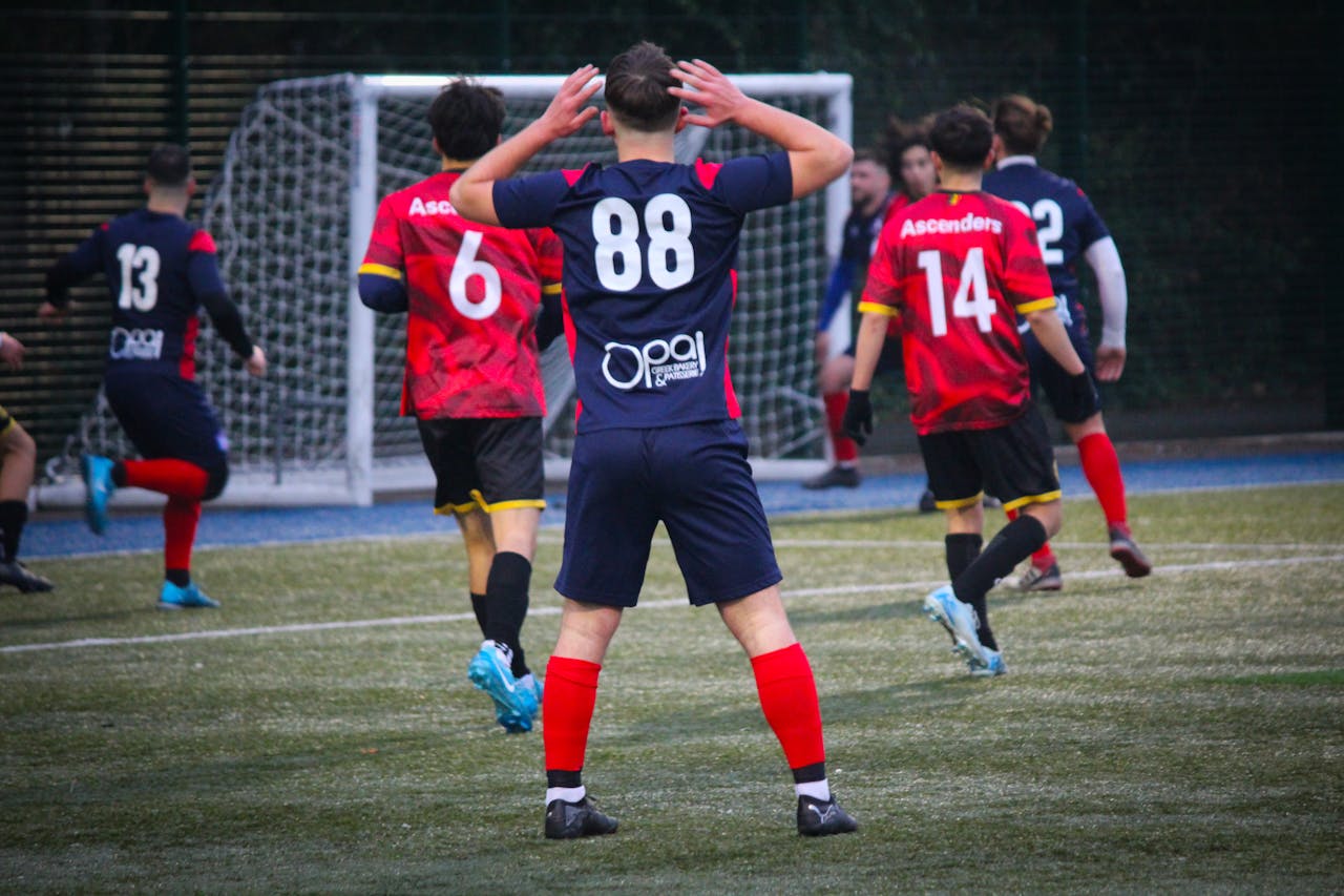 Amateur football players compete on artificial turf during daytime.