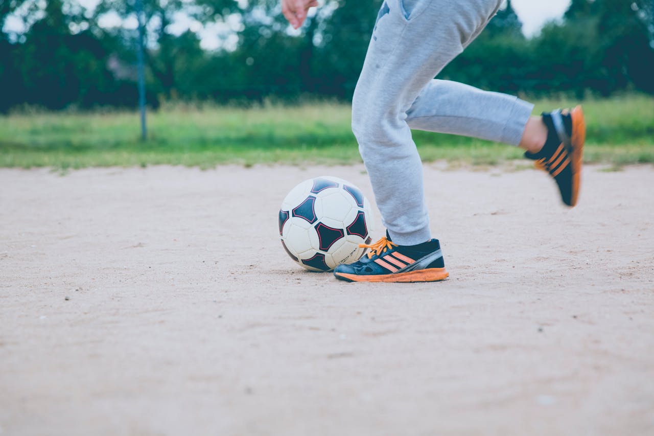 Young player practicing soccer on a sandy outdoor field, capturing motion and fun.